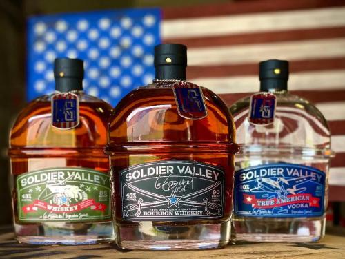 Soldier Valley Spirits (three bottles - whiskey, bourbon, and vodka - displayed in front of an American flag)