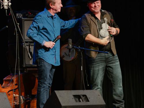 Stuart Duncan (left) congratulates Jim VanCleve after presenting him with his National Fiddler Hall of Fame award at the Appalachian Theatre of the High Country in Boone, North Carolina, on October 4, 2026.  Photo credit: Jamey Booher Photography