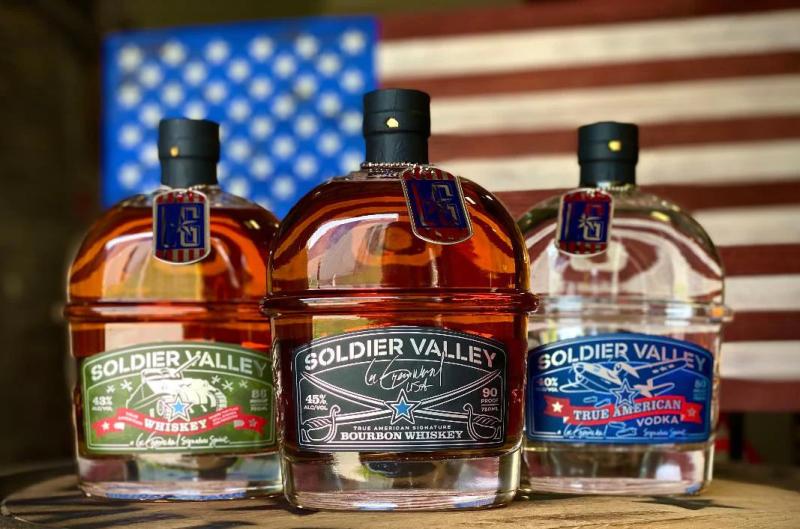 Soldier Valley Spirits (three bottles - whiskey, bourbon, and vodka - displayed in front of an American flag)